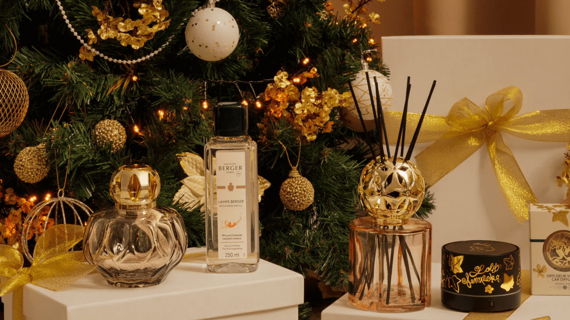 Decorative items including a diffuser, bottles, and candles in front of a Christmas tree.